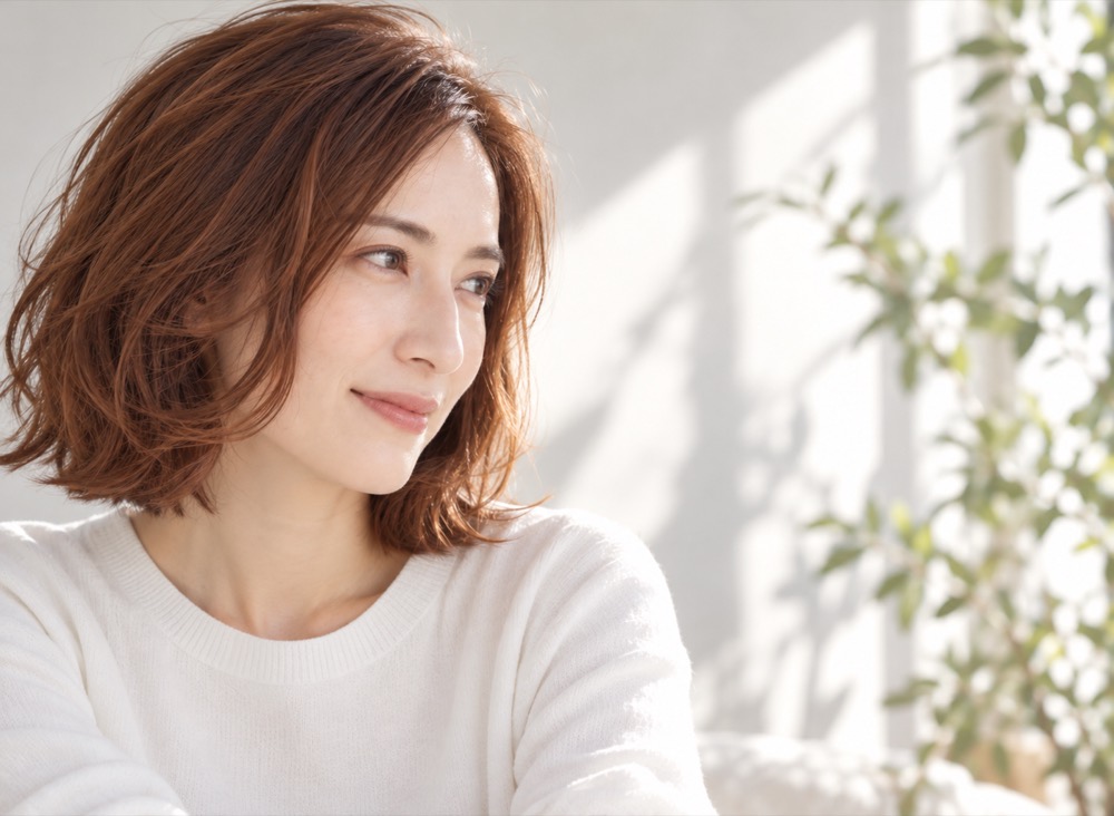 白いニットの女性が横を向いて微笑む、自然な丸みのブラウンボブ